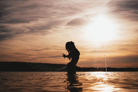 Beauty Model Girl Splashing Water with her Hair. girl Swimming and splashing on summer beach over sunset. Beautiful Woman in Water.