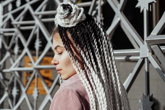 Young woman with futuristic looks. Girl with black and white dreadlocks or pigtails. Against the background of a futuristic building