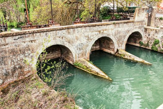 The Jucar River and old stone bridge surrounded by vegetation in Alcala del Jucar village
