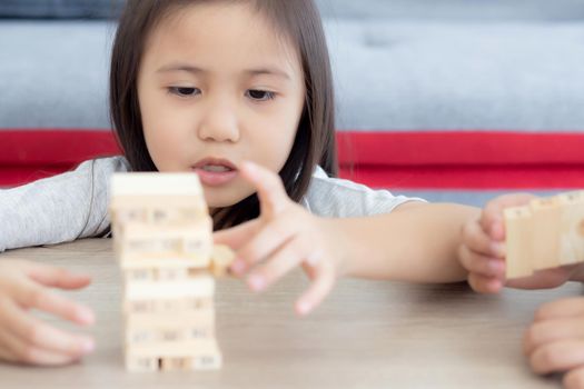 Asian little girl playing game build wood toy with friends on table at home, children concentration and creative for learning, imagine and development and constructor, education and lifestyle concept.