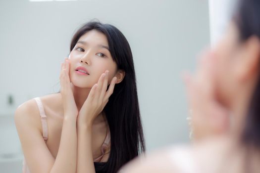 Beautiful young asian woman smiling look at mirror of checking face with skin care and cosmetic for rejuvenation and hygiene, beauty girl happy clean facial with cream or lotion and for health.