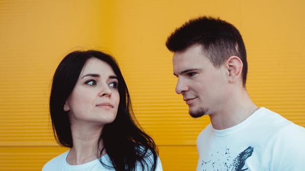 Portrait of a cheerful young couple standing over yellow background - The guy looks at the girl, the girl looks into the distance