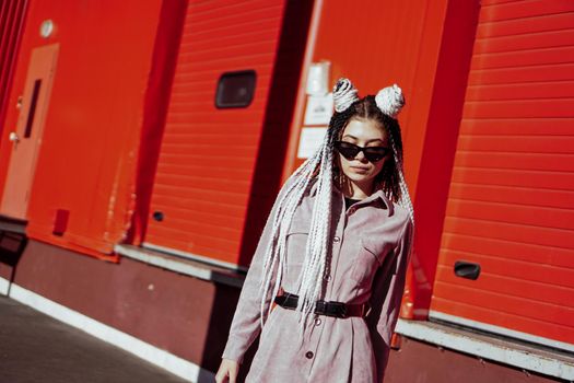 Portrait of beautiful cool girl over urban wall. Sunny day. Girl in sunglasses and pink jumpsuit