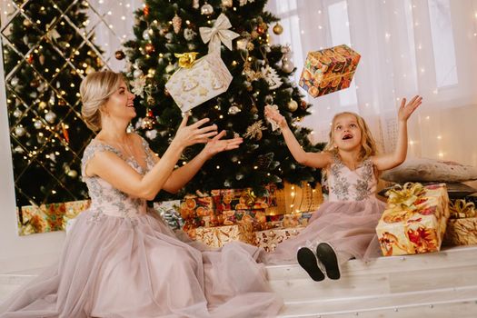 Happy mother and daughter sitting near christmas tree and throwing up gift boxes