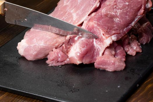 Slice the pork or beef with a knife on the table in close-up. Preparation of meat dishes and food products. Pieces of red meat for shish kebab, barbecue or kebab. Raw fresh meat is cut with a knife