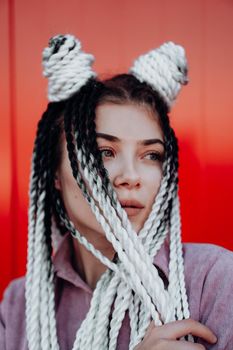 Portrait of beautiful cool girl with Senegalese pigtails and dreadlocks over red wall