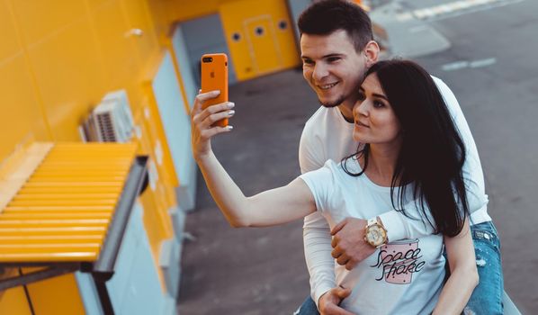 Young lovely couple posing together while making selfie on smartphone over yellow background