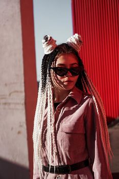 Portrait of beautiful cool girl over urban wall. Sunny day. Girl in sunglasses and pink jumpsuit