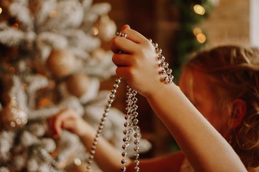 Girl decorates the christmas tree with beads. Selective focus on a small children hand