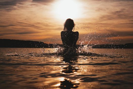 Young model swimming in the sea - sunset time. Feminine, attractive silhouette with spray