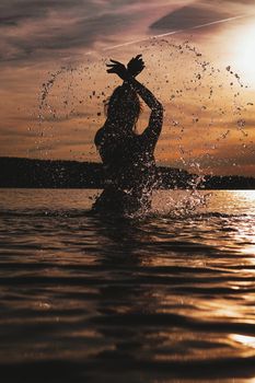 Young model swimming in the sea - sunset time. Feminine, attractive silhouette with spray