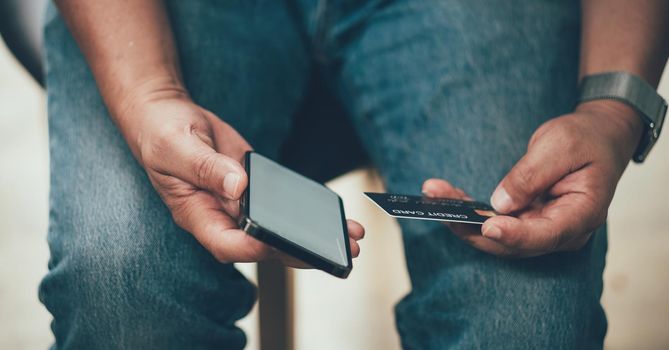 Online payment, Man's hands holding a credit card and using smart phone for online shopping at coffee cafe shop.