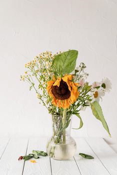 Autumn concept. A bouquet of withered dry flowers and a sunflower in a vase