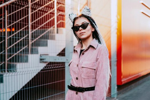 Portrait of beautiful cool girl over urban wall. Sunny day. Girl in sunglasses and pink jumpsuit