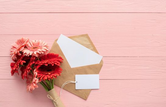 Happy birthday. Red gerbera daisy flowers, envelope and blank label tag on pink wooden table