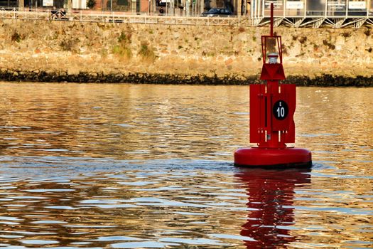 Red signaling beacon floating in the Douro River in Porto. Promenade in the background