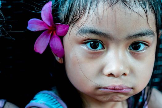 Little girl with large pink flower behind ear. Pretty asian child portrait with flower behind ear