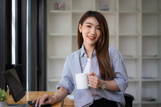Young beautiful woman holding coffee cup and feeling fresh while sitting at her working place at monday morning
