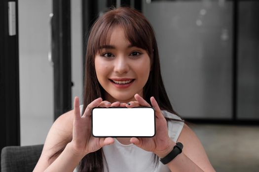 Young asian smiling woman hand holding and showing mobile smart phone with blank white screen, Clipping path. Mockup Concept.