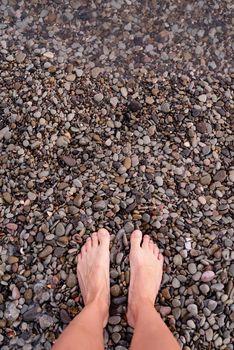 Top view of bare female feet on pebble stones beach