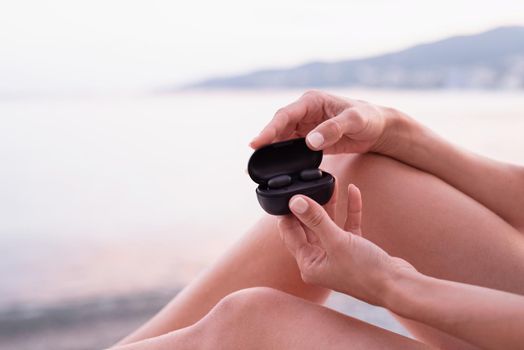 Woman sitting on the sun lounger opening a box with wireless earpieces, ready for listening to the music