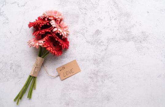 Happy birthday. Red gerbera daisy flowers and craft label tag with words With Love on concrete table, flat lay