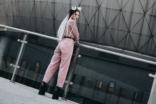 Young woman with futuristic looks. Girl with black and white pigtails standing with her back. Against the background of a futuristic building