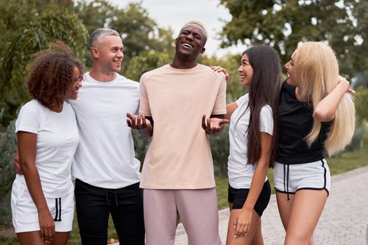 Multi-ethnic group teenage friends. African-american asian caucasian student spending time together Multiracial friendship Happy smiling People dressed black white sportswear meeting outdoor