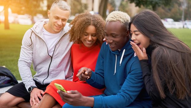 Multi ethnic friends outdoor looking smartphone screen. Diverse group people Afro american asian caucasian spending time together Multiracial male female student sitting bench park outdoors