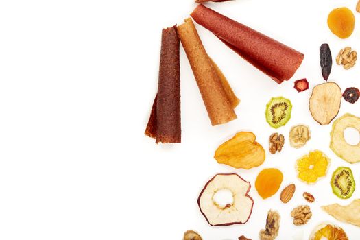 Above view of tasty lozenge with fruits and berries at table and dried fruits kiwi, orange, apple, apricot and bananas on white background. Concept of healthy assorted dried fruit for snacks.