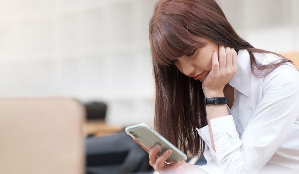 Young woman in white sitting using your smartphone In the background is a library, girls check email, blog, chat, students study online.