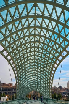 Modern stylish design made of glass and metal, pedestrian bridge over the Kura river in Tbilisi. Tbilisi, Georgia - 03.17.2021