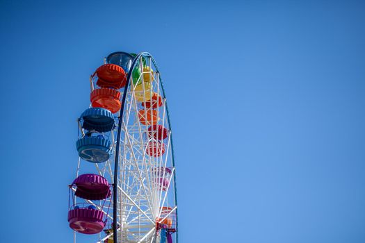 A large Ferris wheel against a blue sky. Booths with people go up. There is a place for the text. Concept: entertainment on summer holidays, holidays with children on weekends, ride on rides.