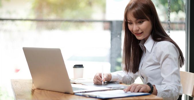 A young, cheerful girl in a white shirt smiles, smiling toothily writing down notes holding training for students to be executives at laptop desktop table