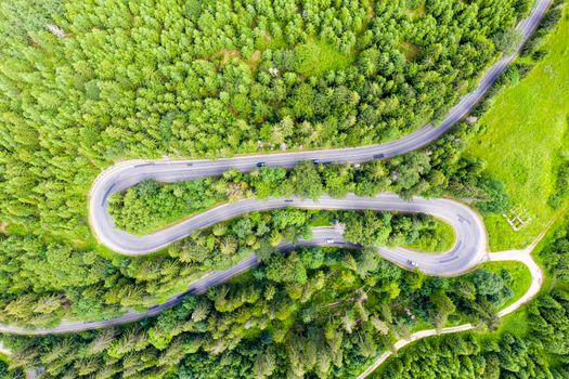 Aerial view of curvy pass road crossing green forest, summer mountain pass scene