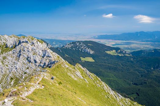 Tourists on trekking path in Piatra Craiului Massif, rocky crest in Romanian Carpathians, summer scene