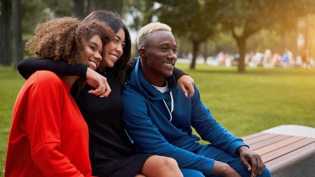 Multi-ethnic group teenage friends. African-american asian student spending time together Multiracial friendship Happy smiling People dressed colorful sportswear sitting bench park outdoor