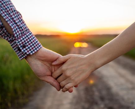 Love concept. A couple holding hand during sunset, a symbol of love and happy relationship. A young couple in love walks through a field at sunset, holding hands and looking at the sunset