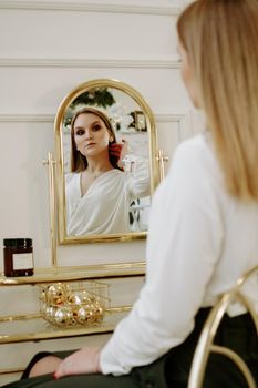 Beautiful woman in a strict white blouse in her room near her dressing table