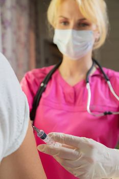 A girl doctor in white gloves makes a vaccination, a vaccine against coronavirus, flu. Coronovirus, disease prevention, Covid-19 of the elderly. Close-up shot in patient's shoulder.