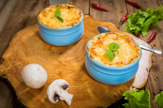 Pots with mushroom julienne on a wooden board, decorated with herbs. Julienne in cocotte with yellow cheese crust.