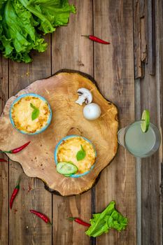 Pots with mushroom julienne on a wooden board, decorated with herbs. Julienne in cocotte with yellow cheese crust. View from above.
