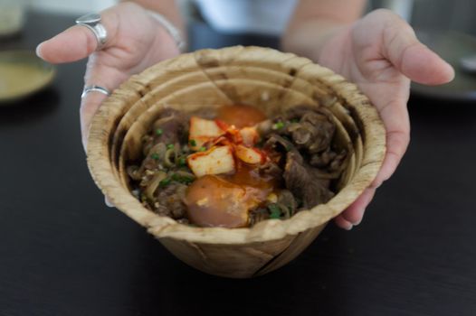 Woman hand with Japanese Gyudon with egg or Japanese beef bowl with egg in organic banan leaf bowl