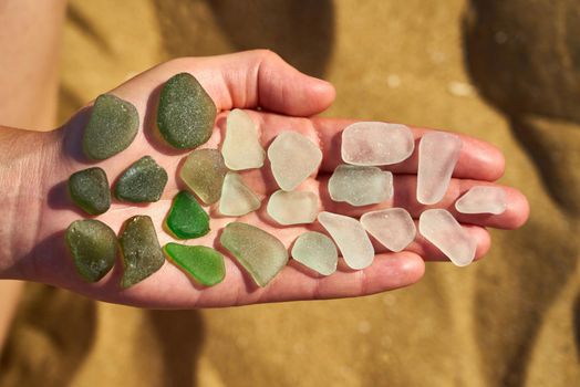 A persons open palm holds sea glass showing the colour gradient from green to white