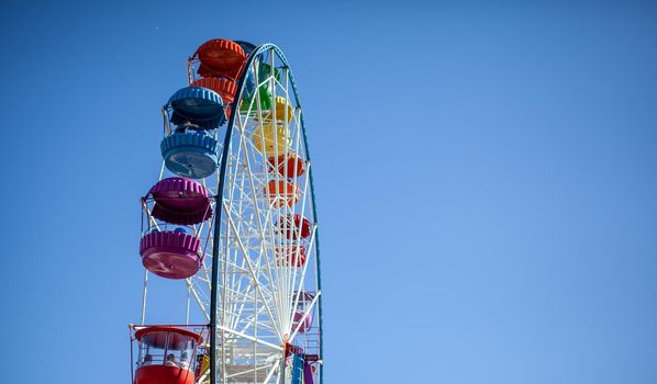 A large Ferris wheel against a blue sky. Booths with people go up. There is a place for the text. Concept: entertainment on summer holidays, holidays with children on weekends, ride on rides.