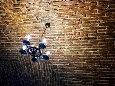 Antique chandelier style with modern lights. It hangs on a red brick ceiling. Rusty look picture.