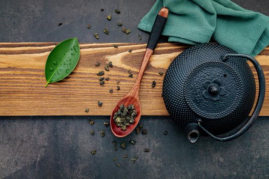 Black cast iron tea pot with herbal tea set up on dark stone background.
