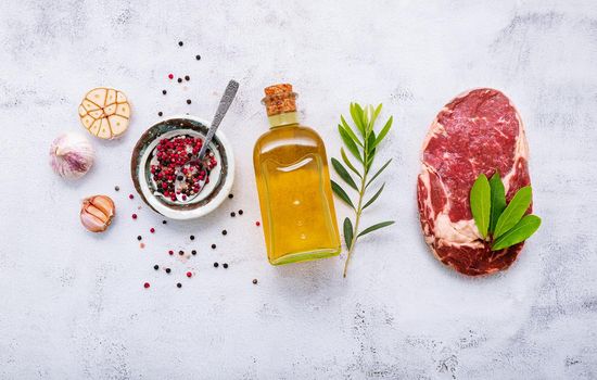 Raw Rib Eye steak set up  on white concrete background. Flat Lay of fresh raw beef steak with rosemary and spice on white shabby concrete background top view.