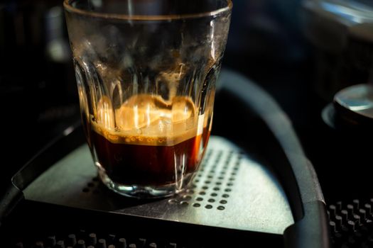 Close focus on double shot of hot espresso coffee on glass cup with dark scene of table.