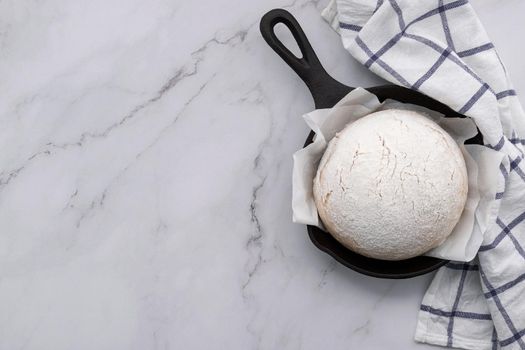 Fresh raw  homemade yeast dough resting in cast iron skillet on marble table flat lay.